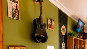 A room with a wooden reception desk, a wall-mounted guitar, a small shelf with decorative items, a wall-mounted TV, and a wooden bookshelf with various items. - Estacion Mendoza Hostel (Mendoza)
