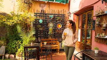 Área de varanda externa com mesa e cadeiras de madeira, um banco e diversos vasos com plantas.