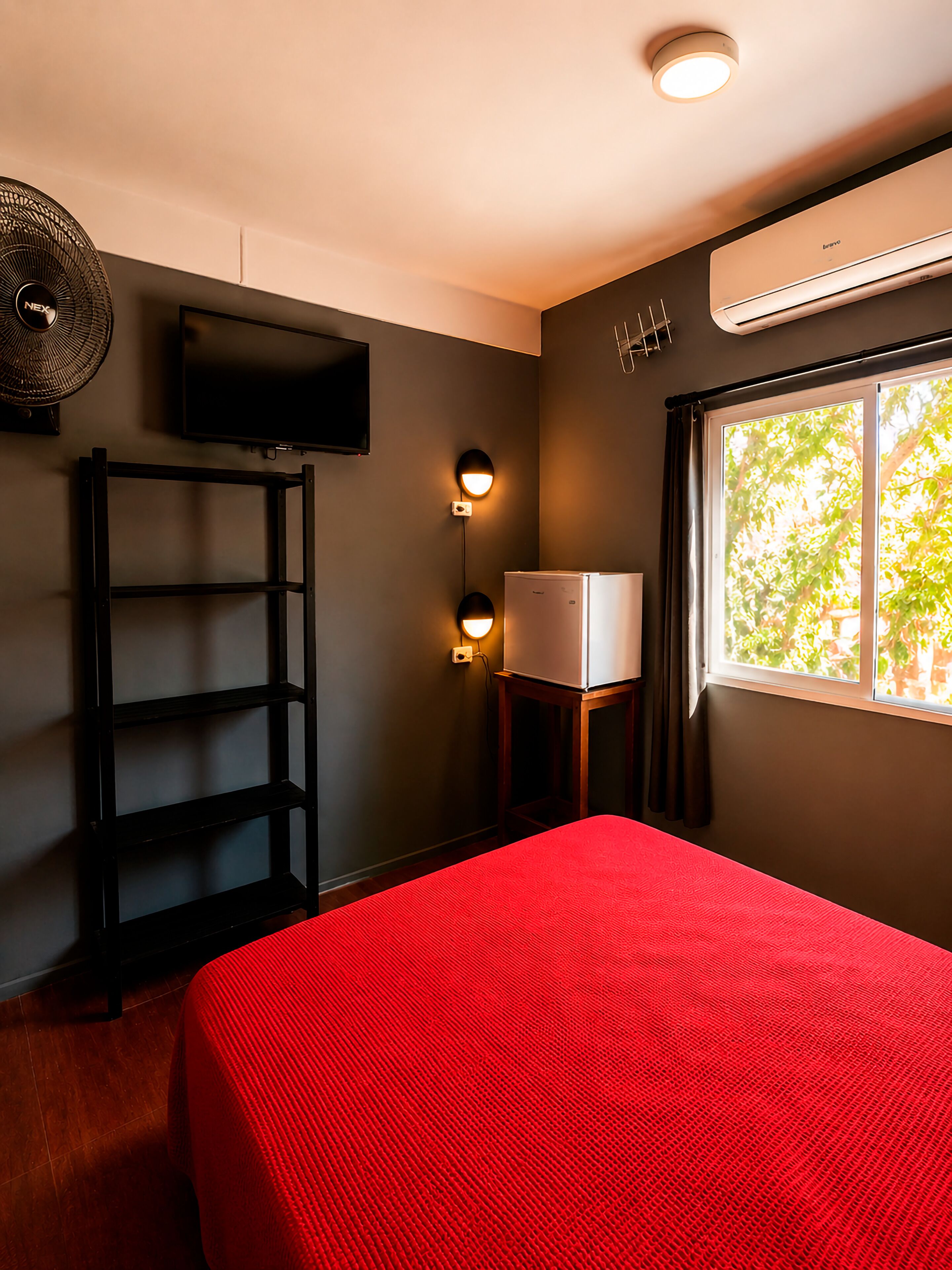 Een kamer met een bed, een televisie, een plank, een wandheater en een raam met uitzicht.