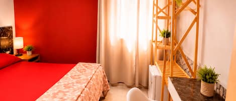 Una habitación con cama, escritorio, silla, televisión y ventana con cortinas.