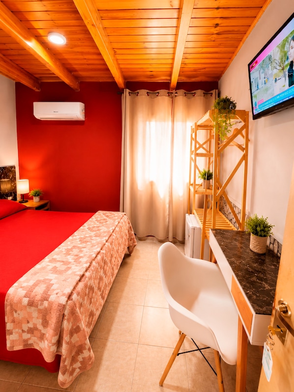 Une chambre avec un lit, un bureau, une chaise, une télévision et une fenêtre avec des rideaux.