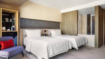A modern bedroom with two beds, a seating area, and a wardrobe.
