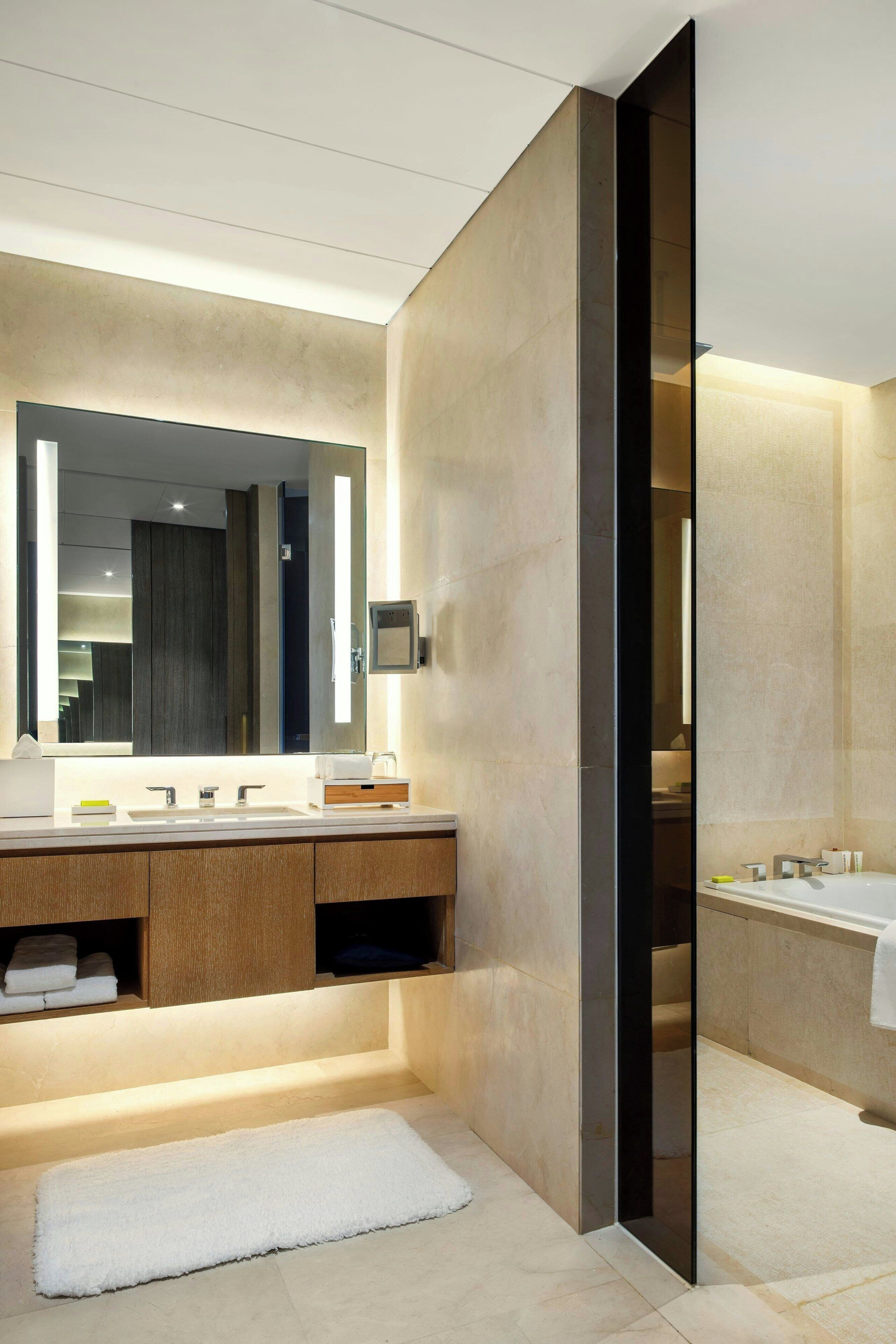 Un baño moderno con un espejo grande, una bañera y un tocador con toallero.