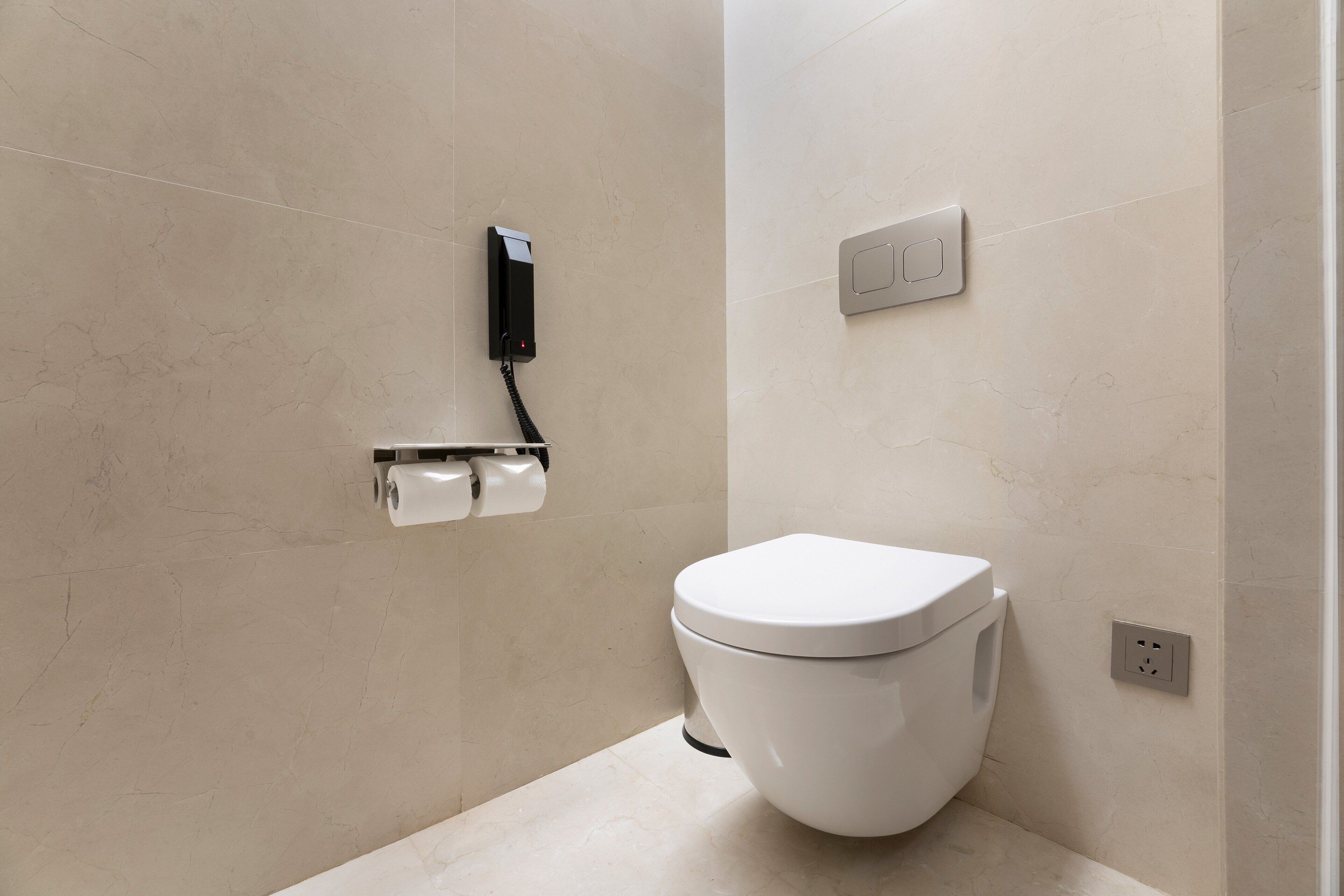 A modern bathroom with a toilet, a paper towel dispenser, and a light switch on the wall.