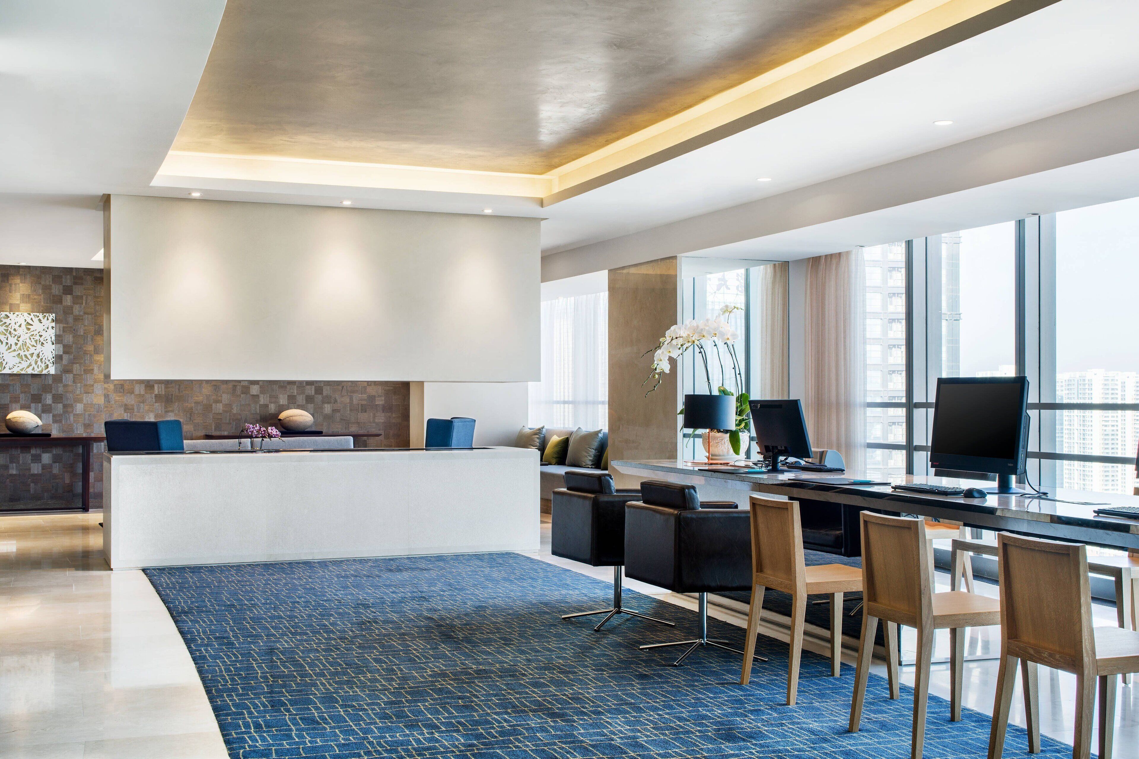 A modern hotel lobby with a reception desk, seating area, and large windows offering city views.