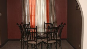 A dining area with a round table and six chairs, a red wall, and a window with sheer curtains. - Cozy Apartments (Kingston)