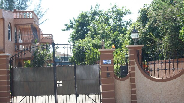 A gated entrance with a wrought iron gate, a brick wall, and a small structure with a lamp post. - Cozy Apartments (Kingston)