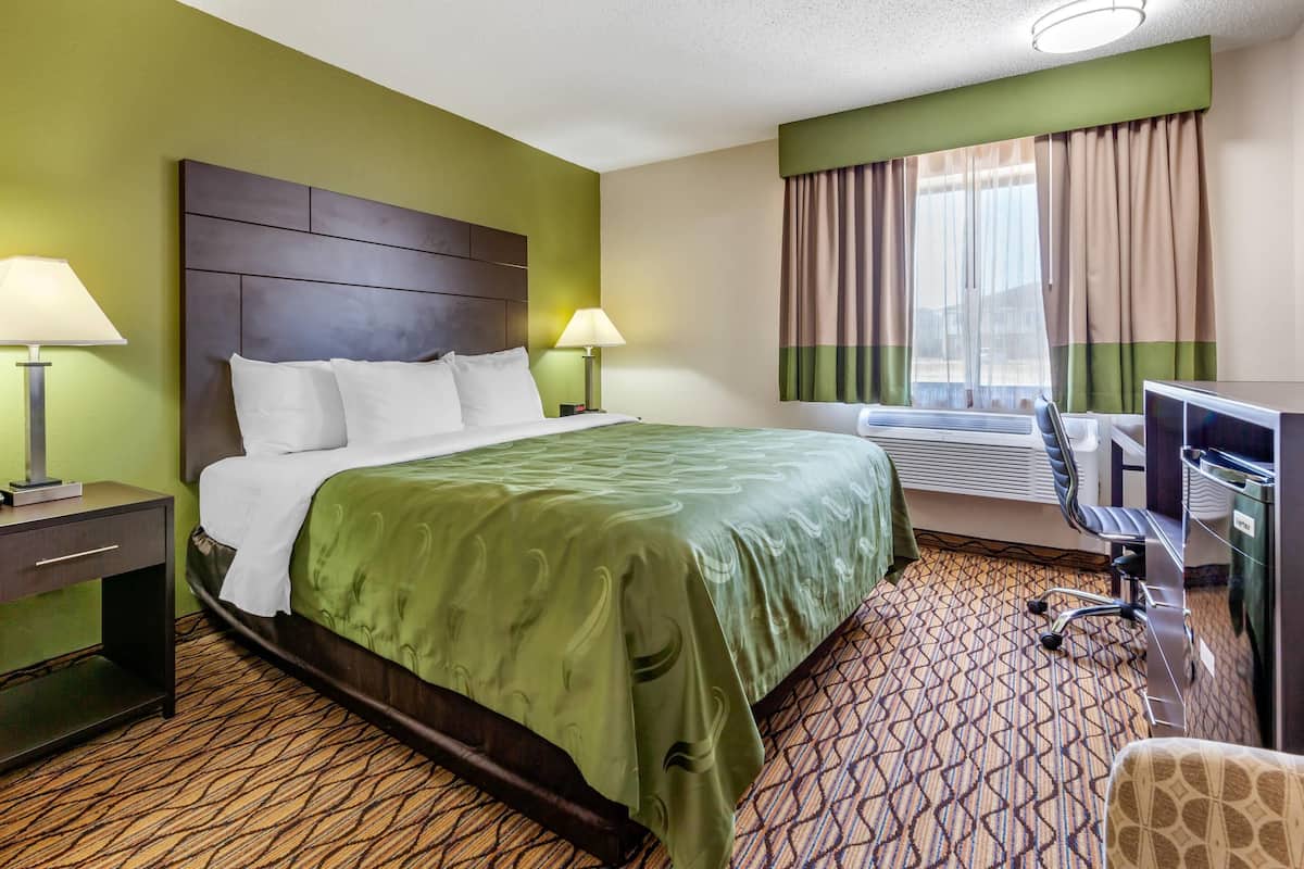 Una habitación de hotel con una cama grande, dos lámparas de noche, un escritorio con silla y una ventana con cortinas.