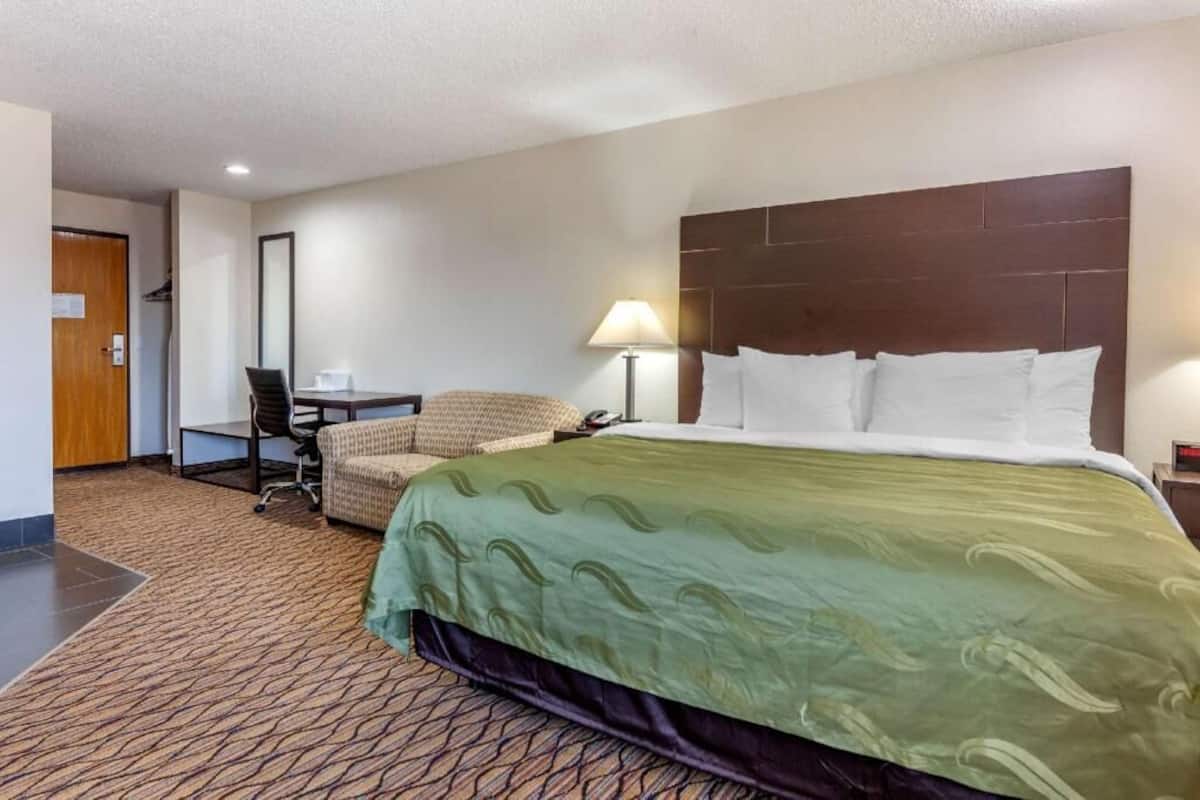 Una habitación de hotel con cama, escritorio, silla y lámpara.