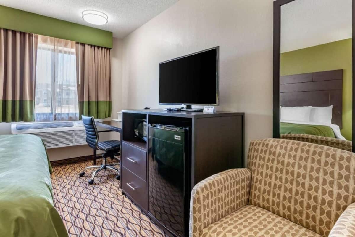 Una habitación de hotel con cama, escritorio con televisor, silla y sofá.