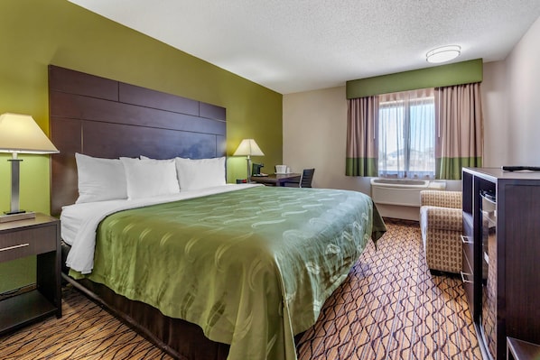 Ein Hotelzimmer mit einem großen Bett, einem Schreibtisch, einem Sessel und einem Fernseher.