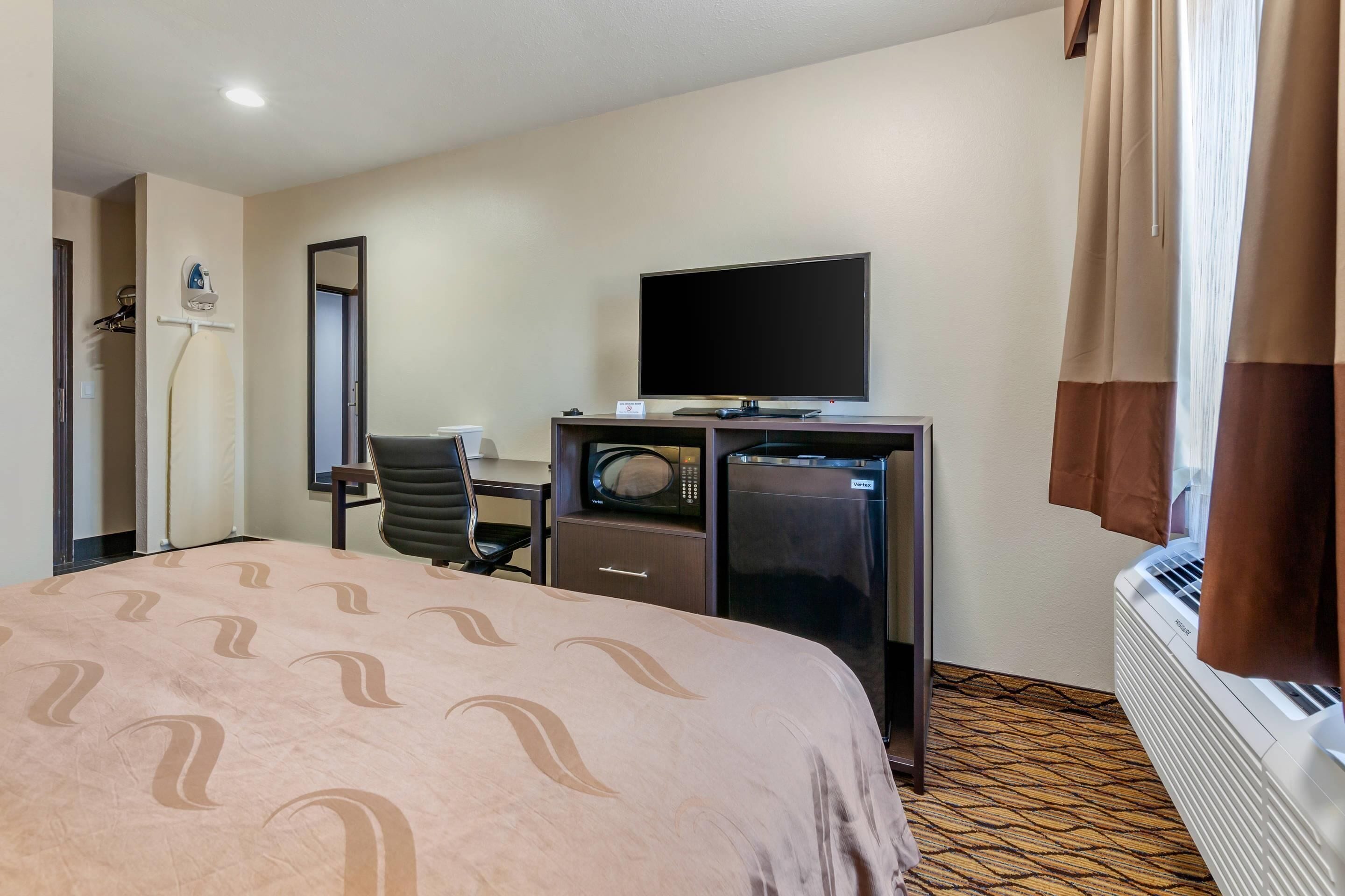 Habitación de hotel con cama, escritorio con computadora, televisor, microondas y refrigerador.