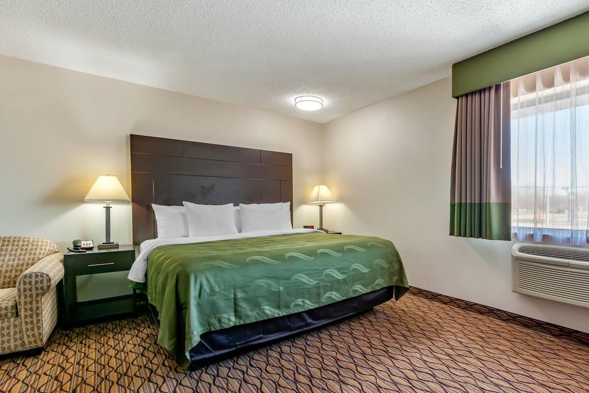 Habitación de hotel con cama, dos lámparas de noche, una silla, mesita de noche y una ventana con cortinas.