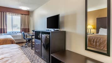 A hotel room with two beds, a desk with a television, a refrigerator, and a mirror reflecting the bed.