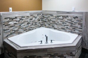 A corner bathtub with a stone mosaic backsplash.