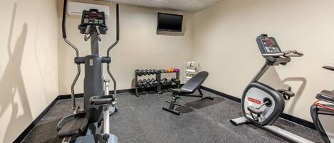 A gym with cardio machines, dumbbells, and a TV on the wall.