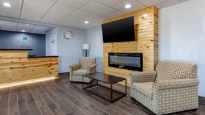 A reception area with a wooden reception desk, two patterned armchairs, a coffee table, a flat-screen TV mounted on a wooden wall, and a clock on the wall. - Quality Inn New London (New London)