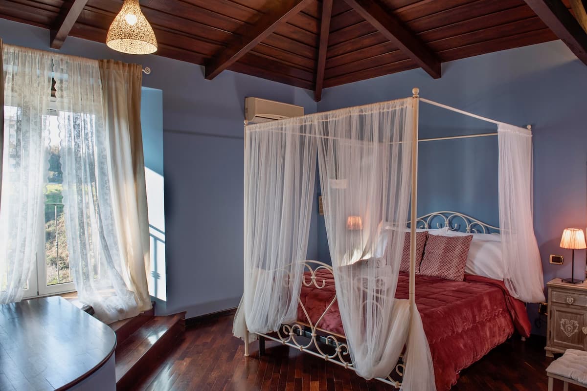 Un lit à baldaquin avec des rideaux légers, un plancher en bois et une fenêtre également ornée de rideaux légers.