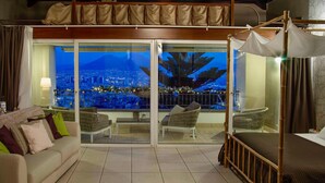 Une chambre d’hôtel avec vue sur la ville, comprenant un canapé, un fauteuil, un lit et un balcon doté d’un auvent.