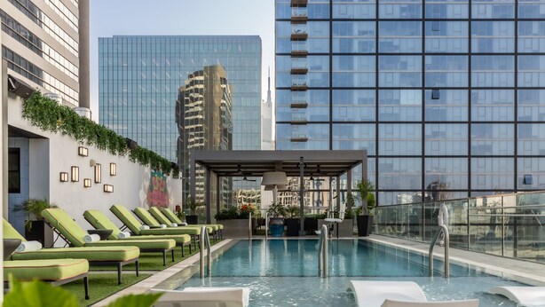 Una piscina en la azotea con sillones de descanso, rodeada de edificios modernos.