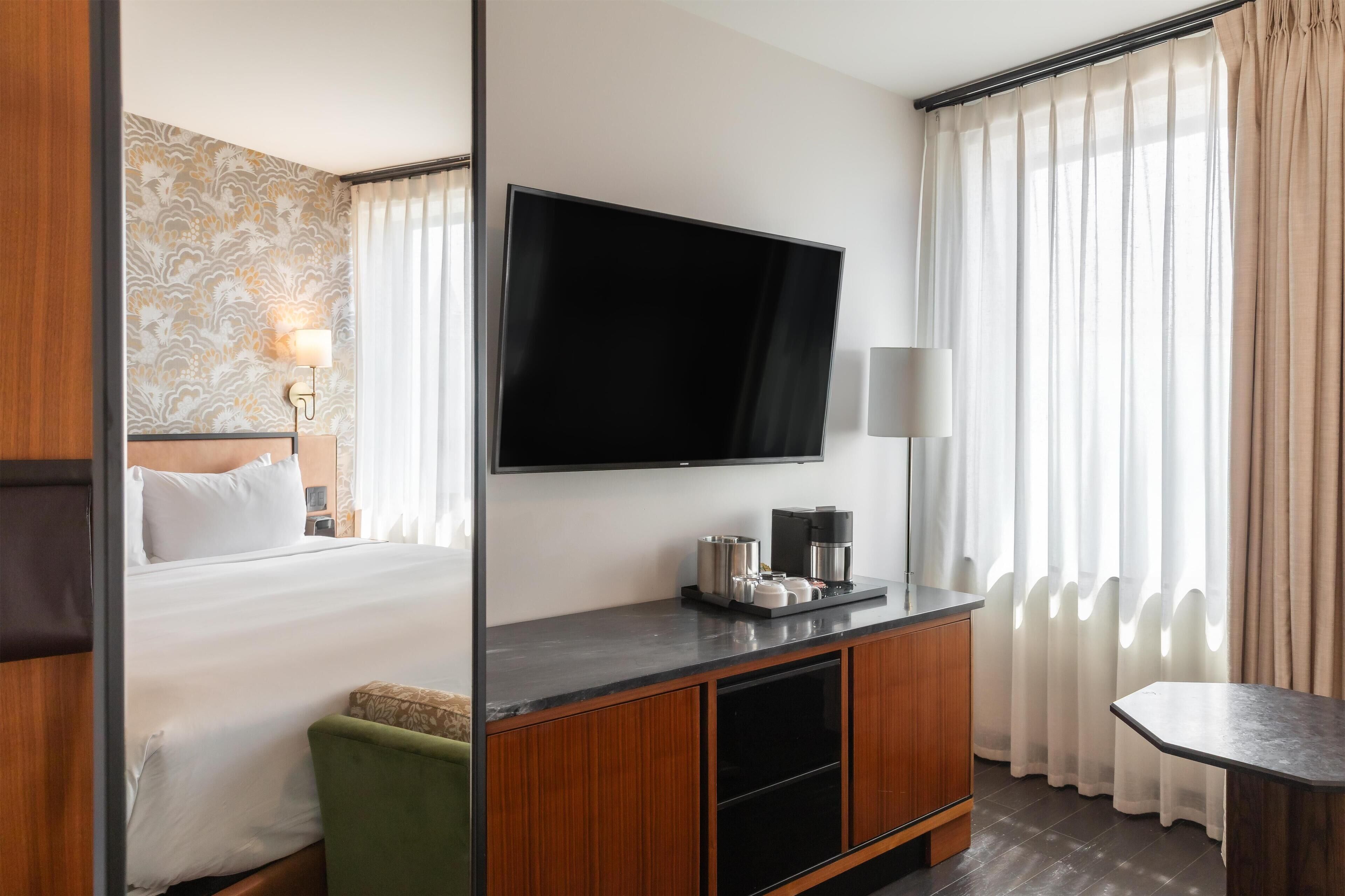 Una habitación de hotel con una cama, televisión, cafetera y escritorio.