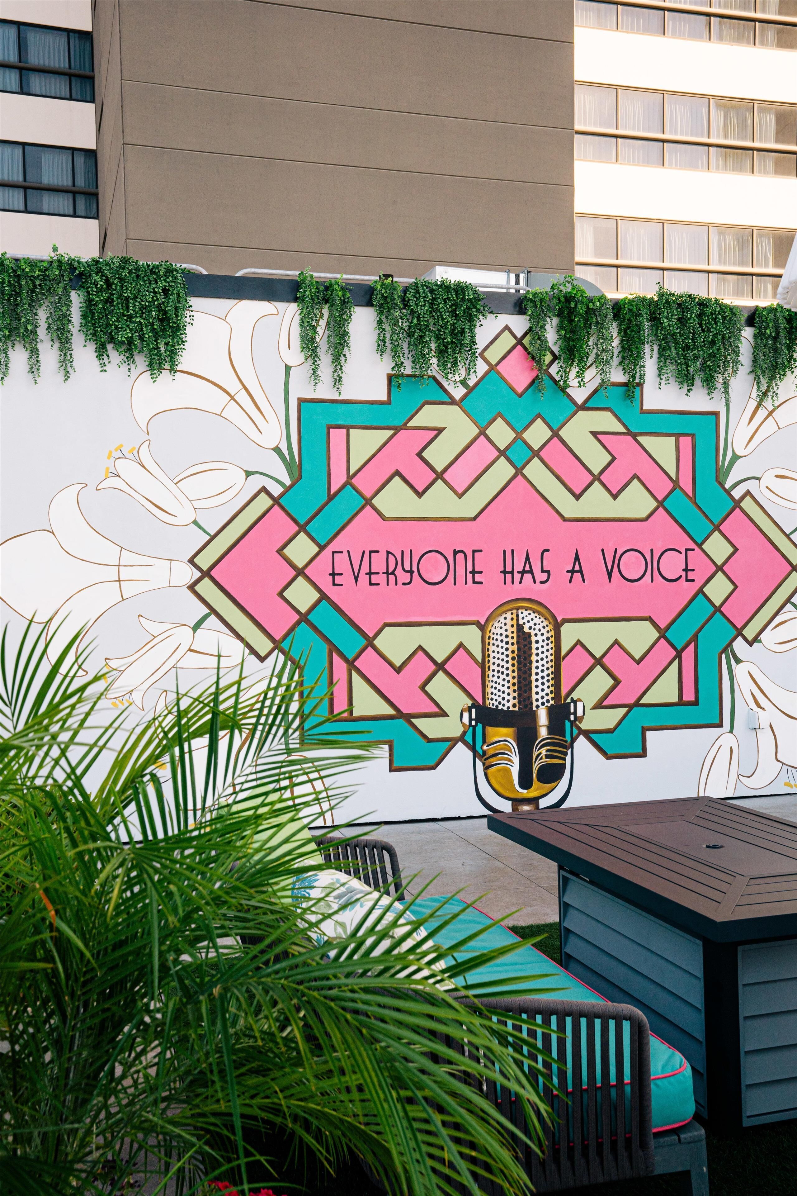 A wall mural with the text "EVERYONE HAS A VOICE" and a microphone, surrounded by greenery and a patterned wall design.