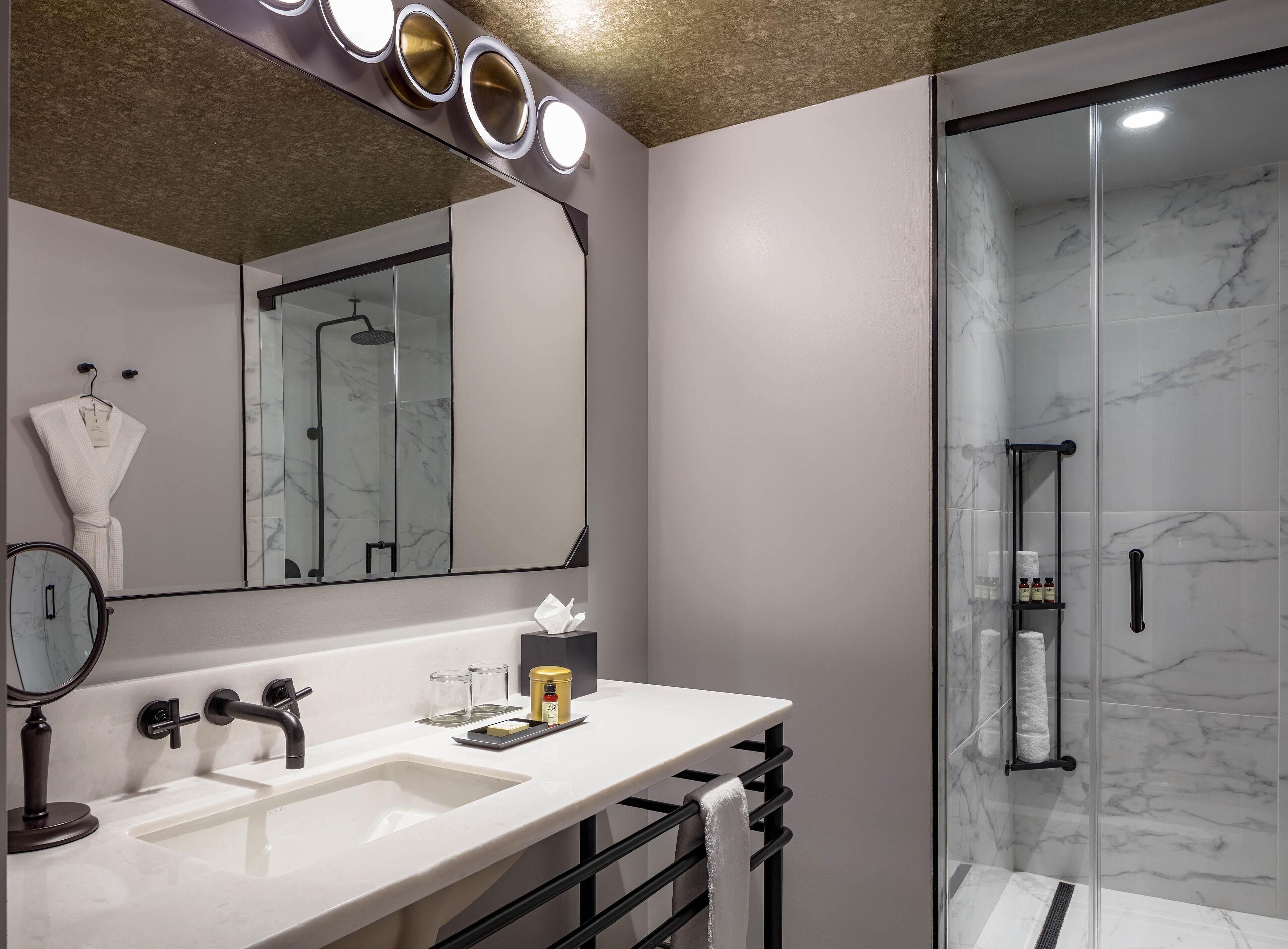 A modern bathroom with a large mirror, a sink, and a glass shower enclosure.