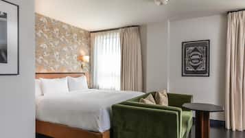 A hotel room with a large bed, a green armchair, a small table, and a wall-mounted lamp.