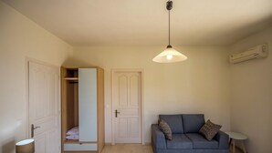 A compact living space with a wardrobe, a sofa, a small table, and a hanging light fixture. - Blue Horizon Studios (Zakynthos)