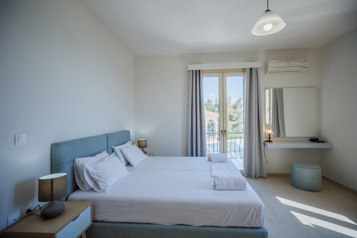 A hotel room with a bed, bedside lamps, a small table, a mirror, and a window with curtains.