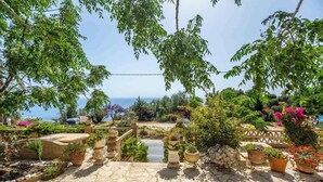 A stone pathway leading to a scenic overlook with a view of the sea, surrounded by lush greenery and potted plants. - Blue Horizon Studios (Zakynthos)