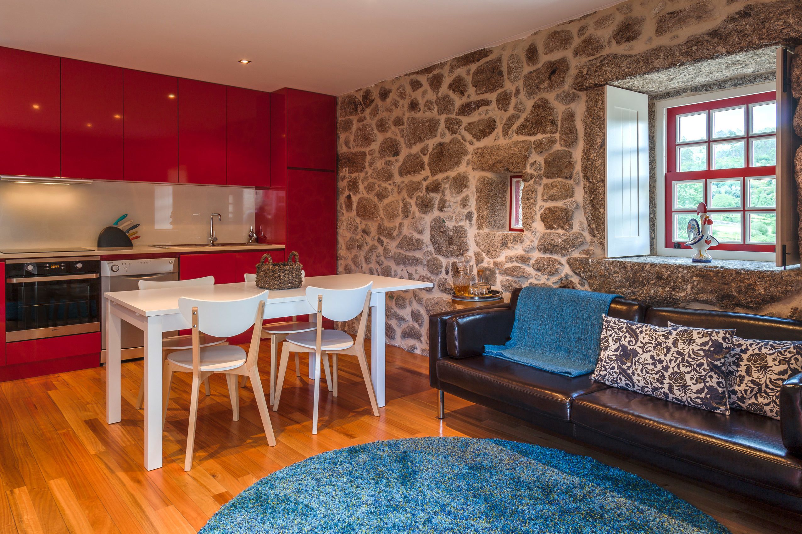 Una cocina moderna con armarios rojos, una pared de piedra y un comedor con una mesa y sillas blancas.
