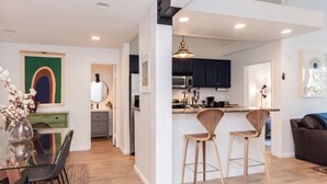 A modern kitchen with dark cabinets, a central island with bar stools, and a dining area with a glass table and chairs. - Crestview B44 (Mammoth Lakes)
