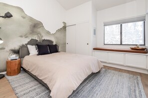 A bedroom with a large bed, a nightstand, a wall with a unique texture, a window with a view, and a wooden bench by the window. - Crestview B44 (Mammoth Lakes)