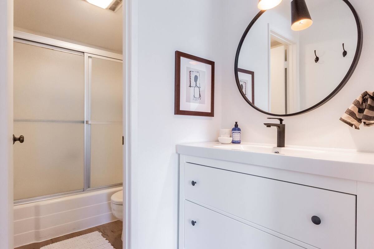 Un bagno con un mobile lavabo bianco, uno specchio rotondo e un quadro appeso alla parete.