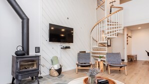 A modern living room with a stone fireplace, a flat-screen TV, two chairs, a wooden coffee table, and a spiral staircase. - Crestview B44 (Mammoth Lakes)