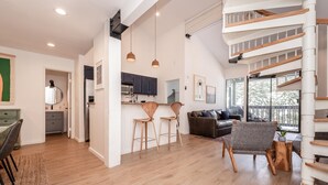A spacious living area with a wooden staircase, a kitchen with dark cabinets, and a dining area with wooden chairs. - Crestview B44 (Mammoth Lakes)