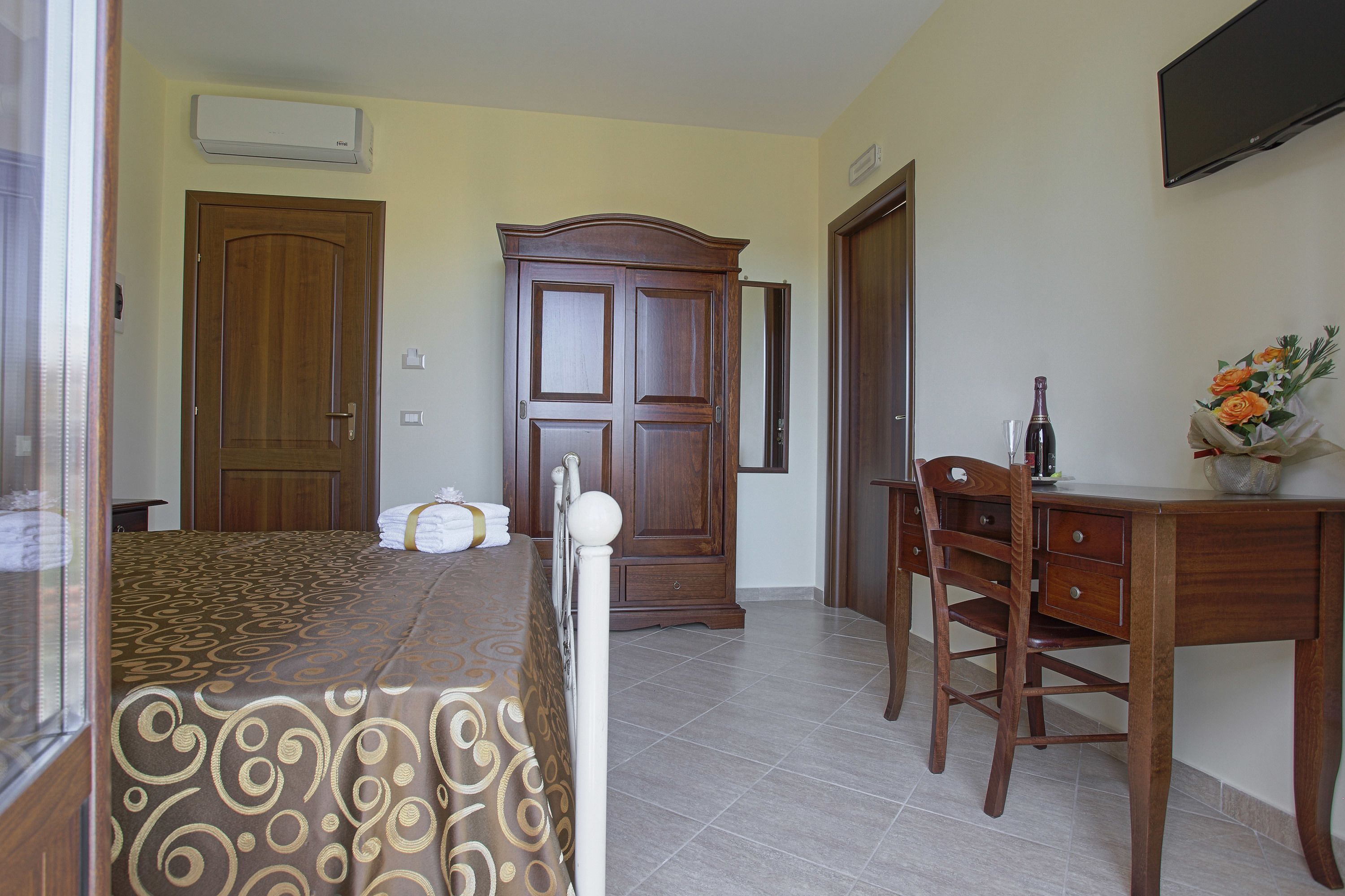 A bedroom with a bed, a wooden wardrobe, a desk, and a chair.