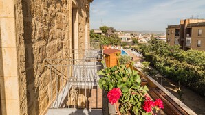 Un balcon avec un mur en pierre, une rambarde en métal et des plantes en pot.