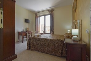 A hotel room with a bed, a desk with a chair, a television, and a window with curtains.