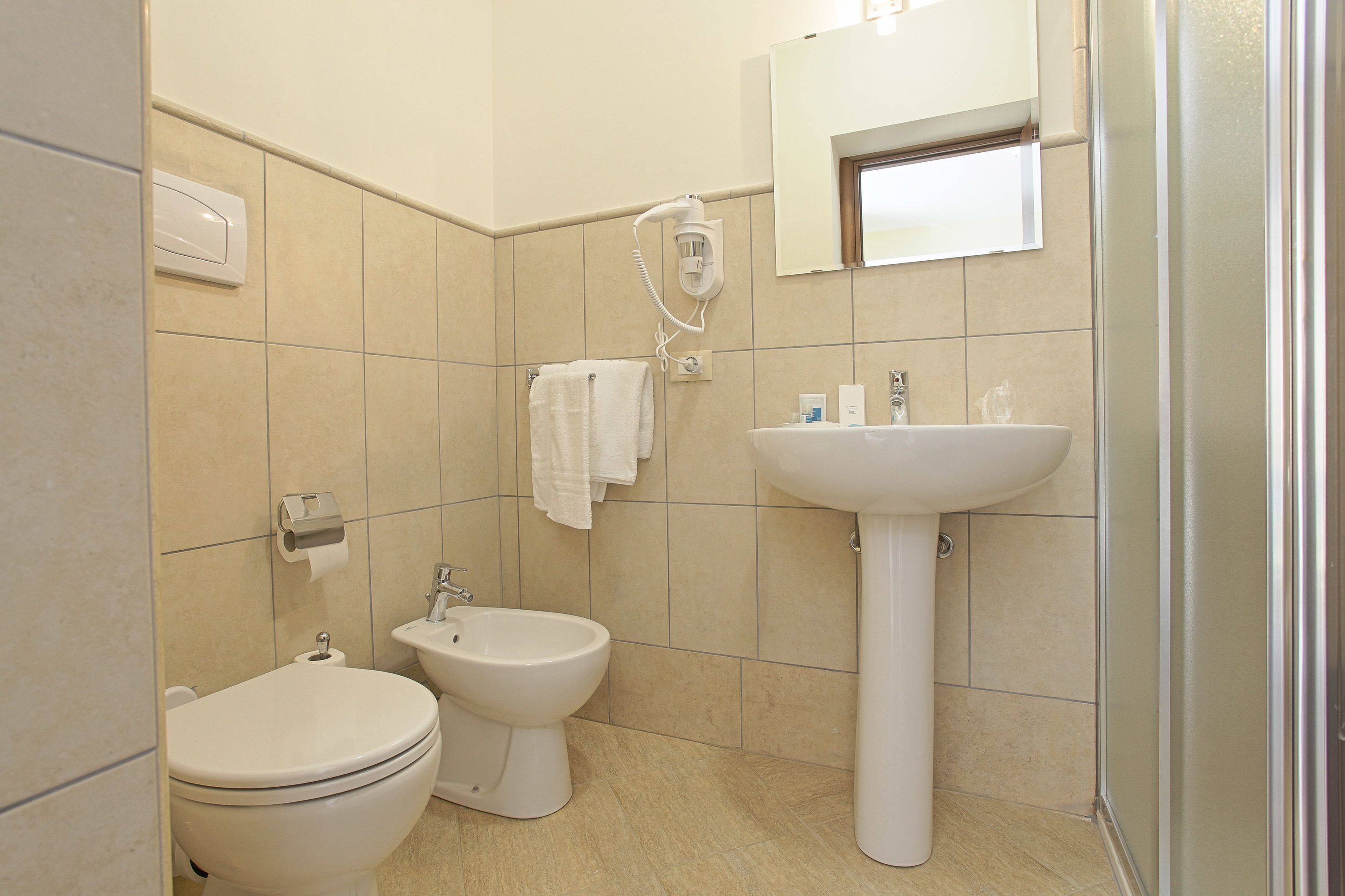 Une salle de bain équipée de toilettes, d’un bidet, d’un lavabo et d’un miroir.
