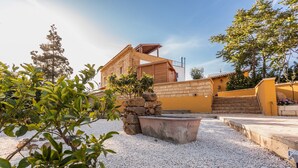 Une cour avec un foyer en pierre, une pergola en bois et un bâtiment jaune avec un escalier menant à un balcon.