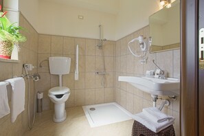 A modern bathroom with a toilet, shower, sink, and a small step for accessibility.