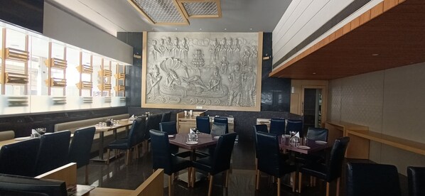 A restaurant with high ceilings, a large mural, and modern seating. - Hotel Gopalas Residency (Bhiwandi)