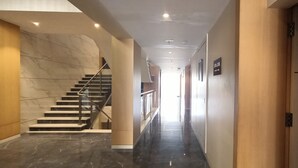 A modern hotel corridor with a marble staircase, a wooden door, and a sign indicating the direction to the lobby. - Hotel Gopalas Residency (Bhiwandi)