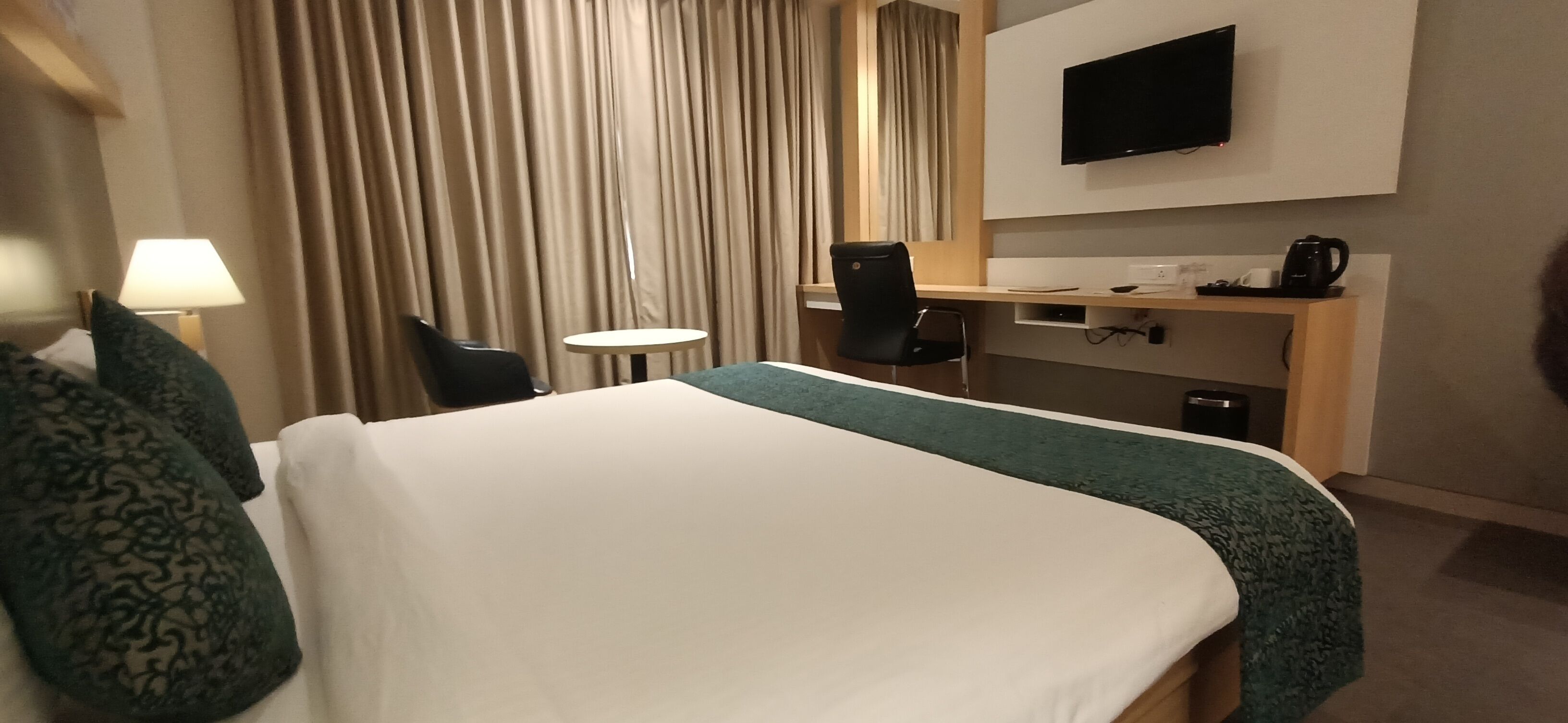 A hotel room with a bed, a desk, a chair, a TV, and a coffee maker.