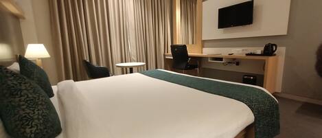 A hotel room with a bed, a desk, a chair, a TV, and a coffee maker.