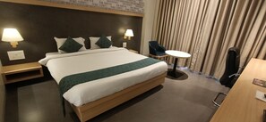 A hotel room with a large bed, two bedside lamps, a small round table, a chair, and a desk. - Hotel Gopalas Residency (Bhiwandi)