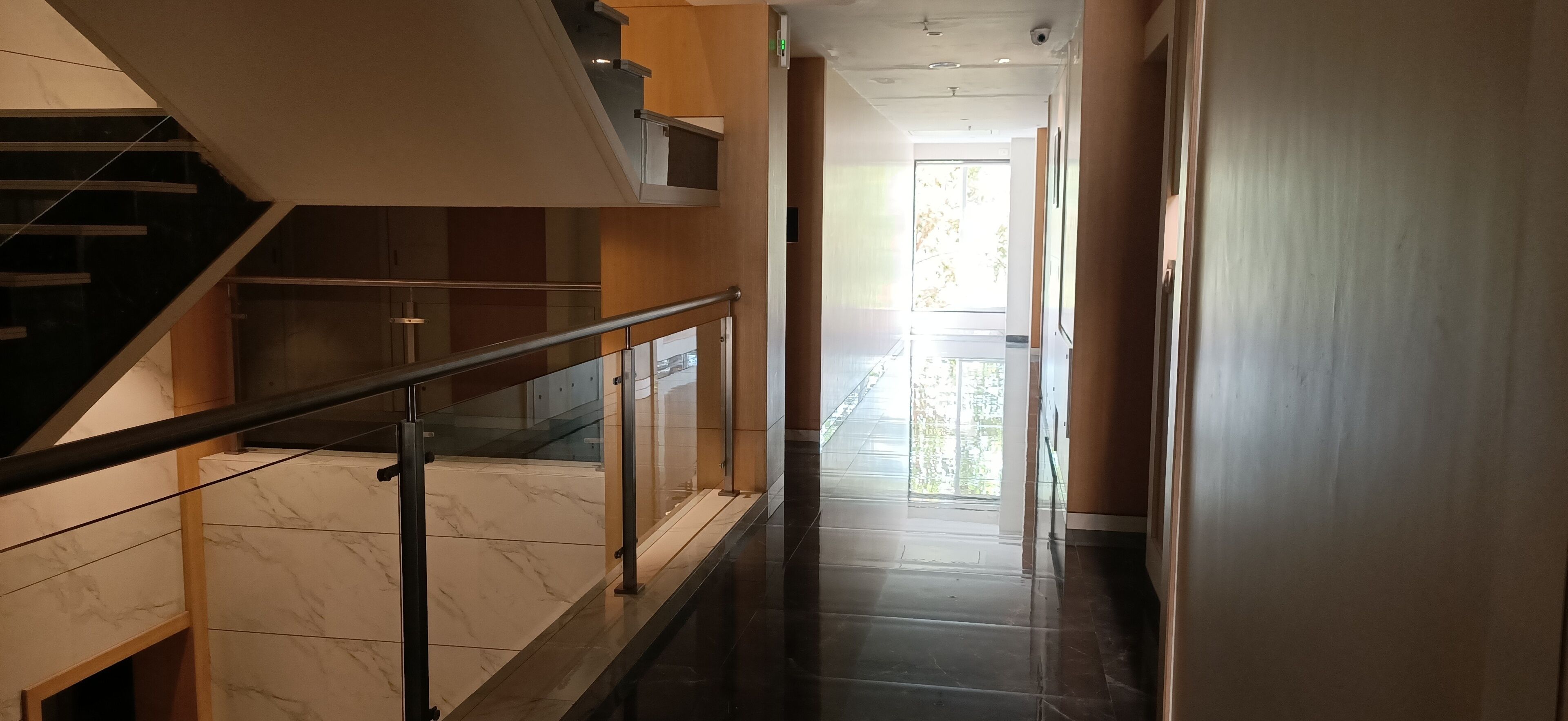 Un interior modern amb una escala de marbre, baranes de vidre i vistes a la vegetació exterior.