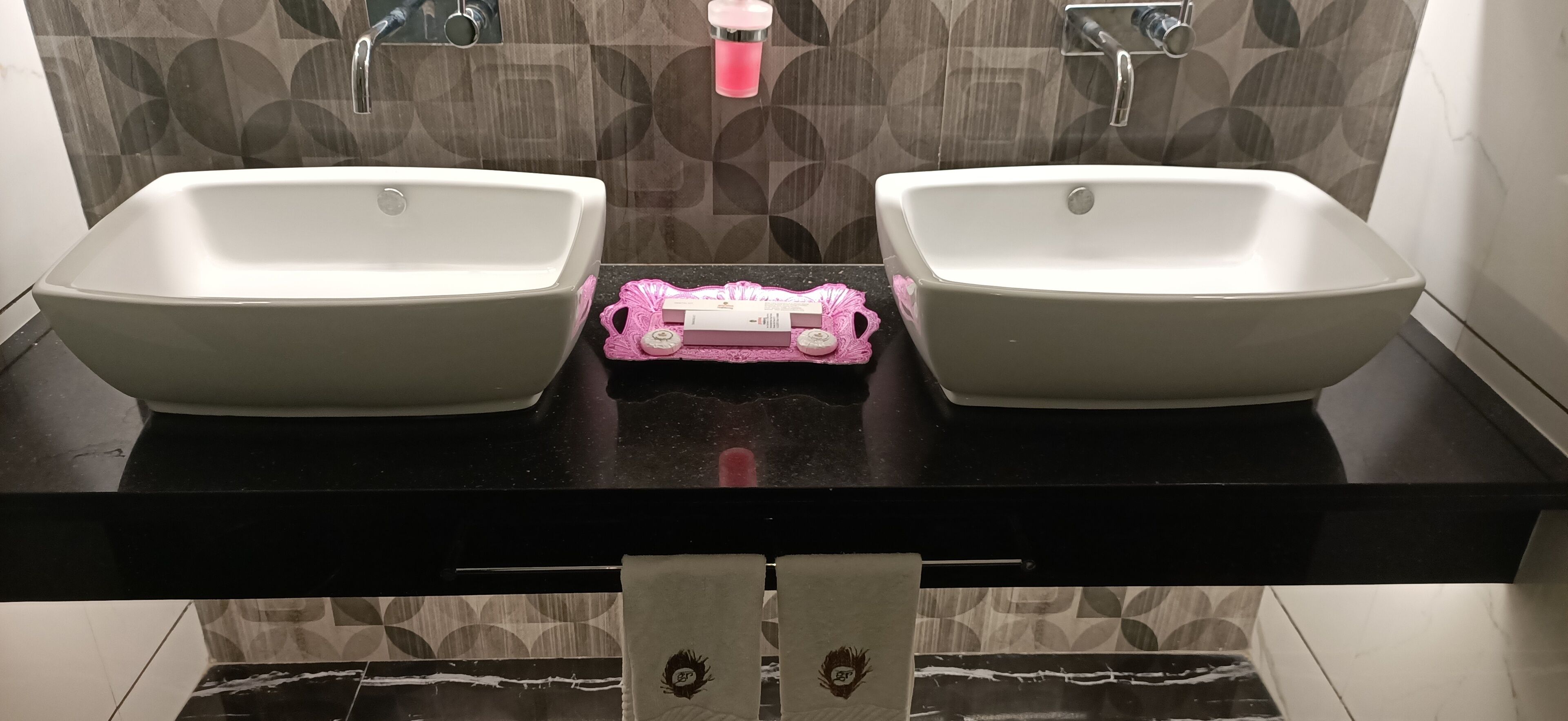 A bathroom with two white sinks, a black countertop, and patterned wall tiles.